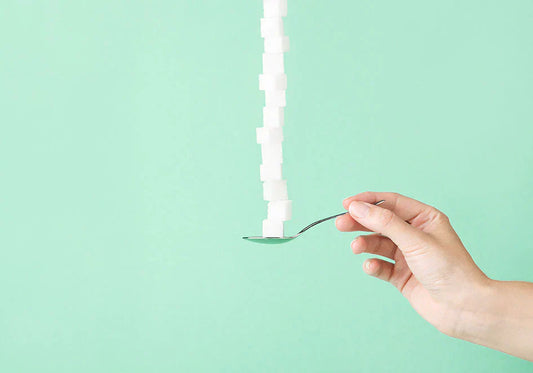 Hand holding spoon stacked with sugar cubes on mint green background