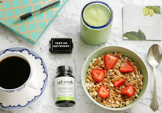 Healthy breakfast with Calocurb supplement, green smoothie, cereal with strawberries, and coffee on a marble table