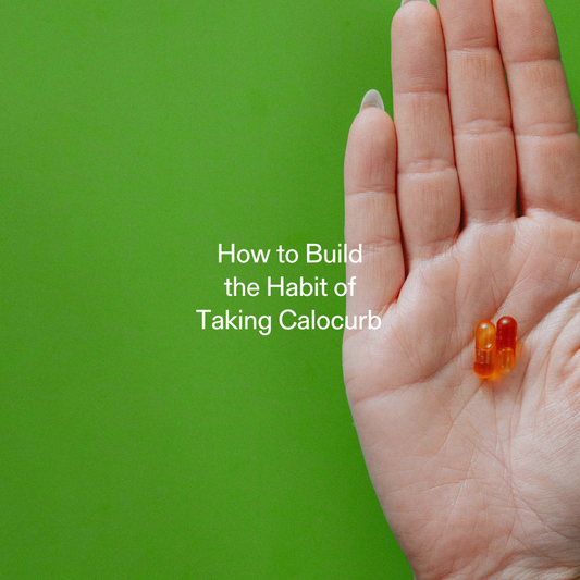 Hand holding two Calocurb capsules against a green background, symbolizing habit formation and daily supplement routine