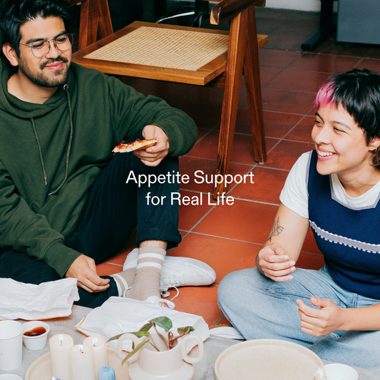 Two adults sitting on the floor sharing pizza with on-image text reading “Appetite Support for Real Life”