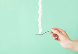 Hand holding spoon stacked with sugar cubes on mint green background