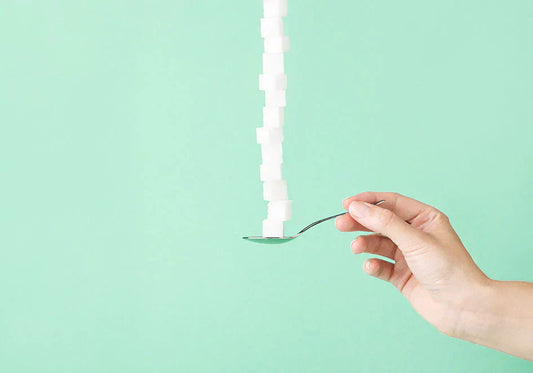 Hand holding spoon stacked with sugar cubes on mint green background