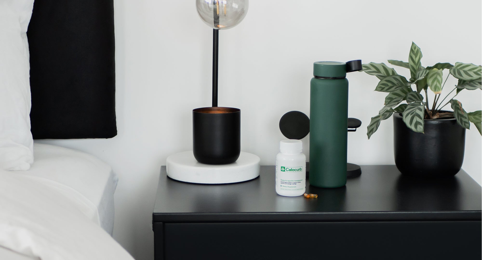 Nightstand with a lamp, water bottle, plant, and bottle of Calocurb.